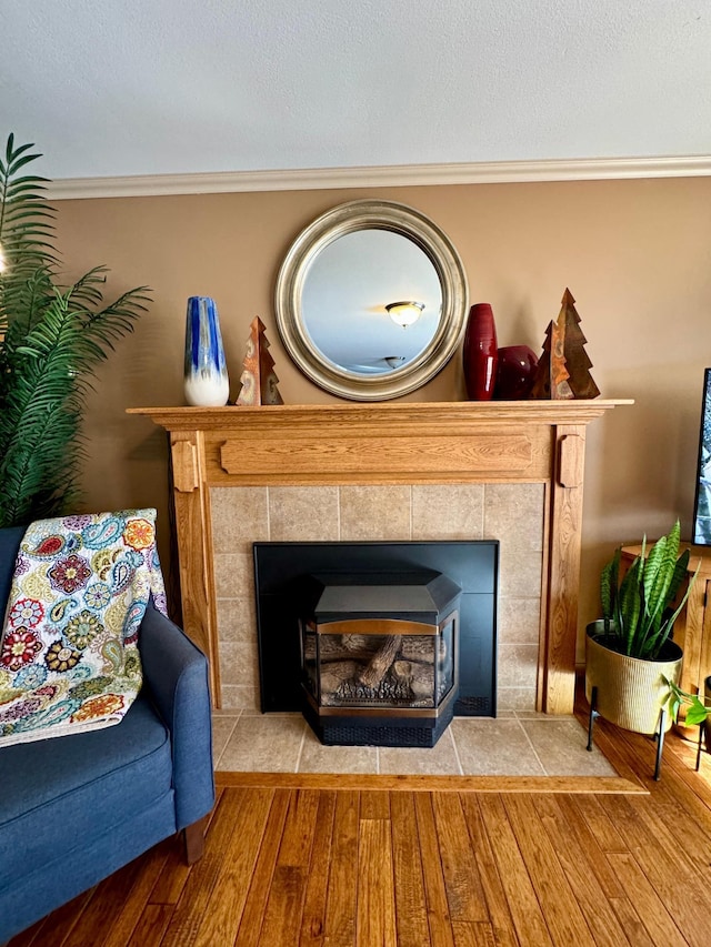 interior details with a textured ceiling, ornamental molding, wood finished floors, and a tiled fireplace