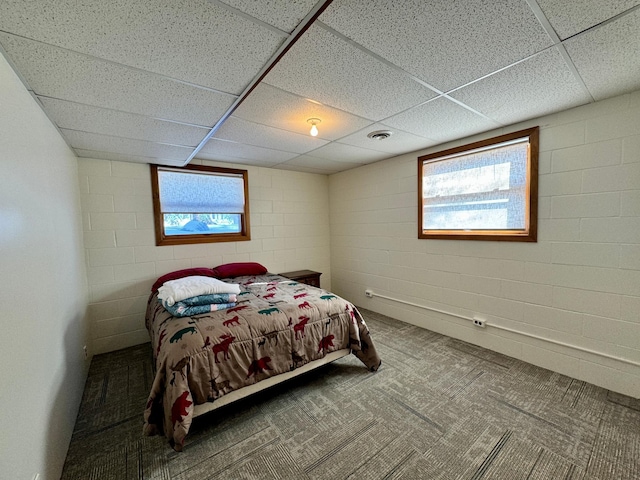 carpeted bedroom featuring a paneled ceiling, multiple windows, visible vents, and concrete block wall