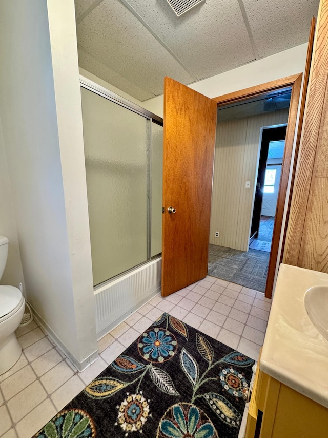 full bathroom featuring a paneled ceiling, toilet, vanity, combined bath / shower with glass door, and tile patterned floors