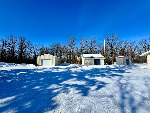 yard covered in snow featuring a garage, a storage unit, and an outbuilding