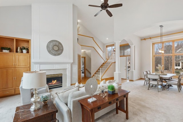 living room with a premium fireplace, ornate columns, ceiling fan, light carpet, and high vaulted ceiling