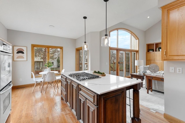 kitchen featuring light wood-style flooring, a kitchen island, a kitchen bar, decorative light fixtures, and stainless steel gas stovetop