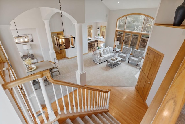 living area featuring high vaulted ceiling, stairway, light colored carpet, and ornate columns