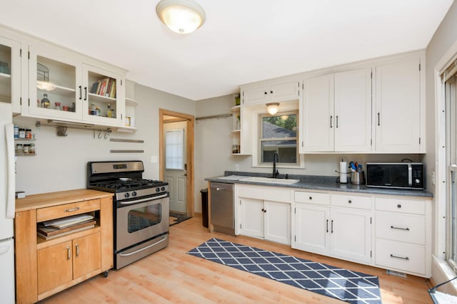 kitchen with dark countertops, glass insert cabinets, appliances with stainless steel finishes, open shelves, and a sink