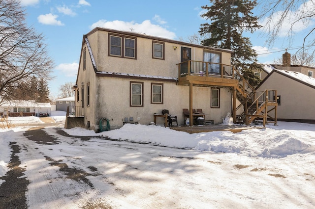 snow covered rear of property with stairs, a balcony, a garage, and stucco siding