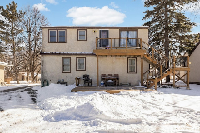 snow covered house with a wooden deck, stairs, and stucco siding