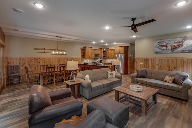 living room featuring a ceiling fan, recessed lighting, a wainscoted wall, and wooden walls