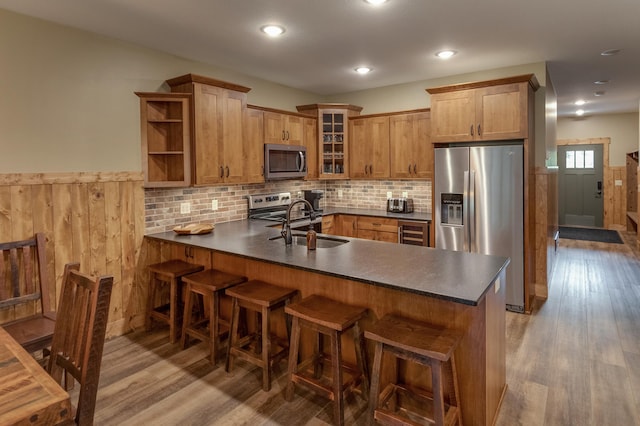 kitchen with wainscoting, dark countertops, glass insert cabinets, a peninsula, and stainless steel appliances