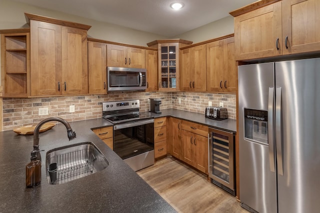 kitchen featuring beverage cooler, decorative backsplash, glass insert cabinets, stainless steel appliances, and a sink