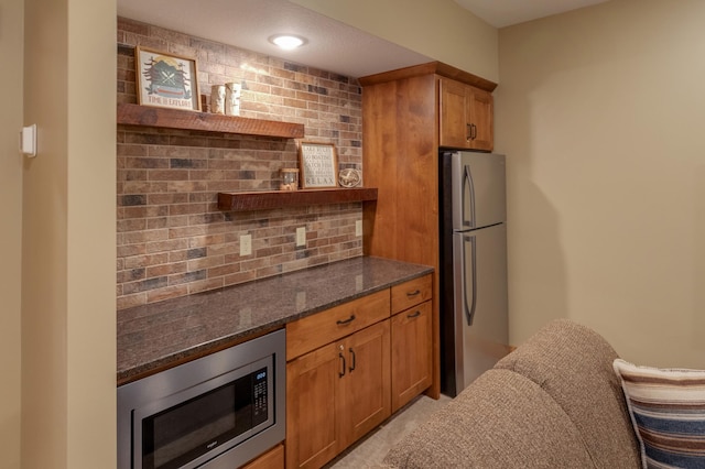 kitchen with brown cabinets, backsplash, stainless steel appliances, and dark stone countertops