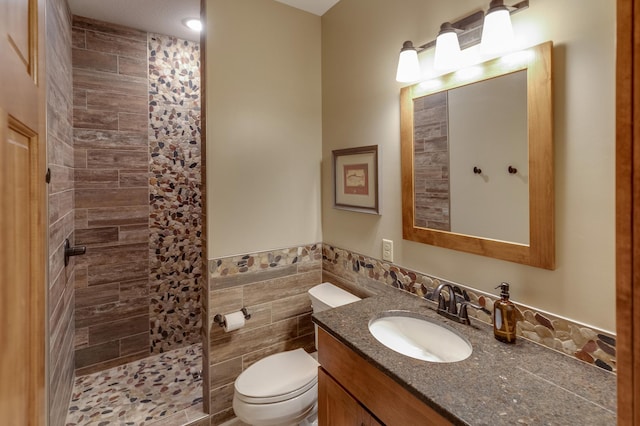 full bath with wainscoting, toilet, vanity, a walk in shower, and tile walls