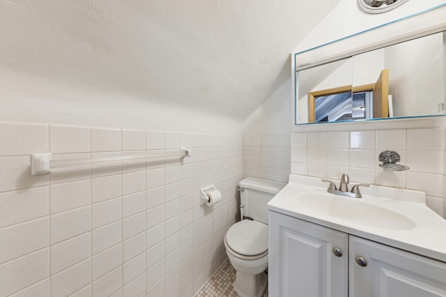 bathroom featuring lofted ceiling, toilet, a textured ceiling, vanity, and tile walls