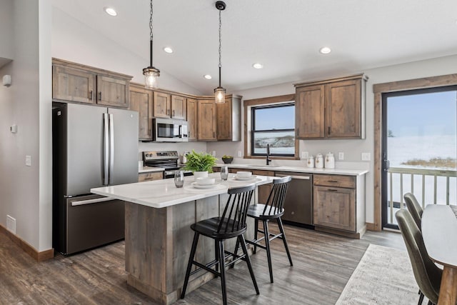 kitchen featuring a center island, decorative light fixtures, sink, vaulted ceiling, and appliances with stainless steel finishes