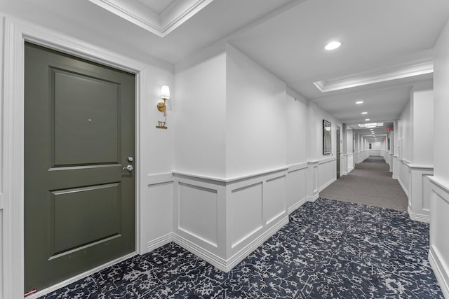 corridor featuring carpet flooring, wainscoting, a decorative wall, recessed lighting, and a tray ceiling