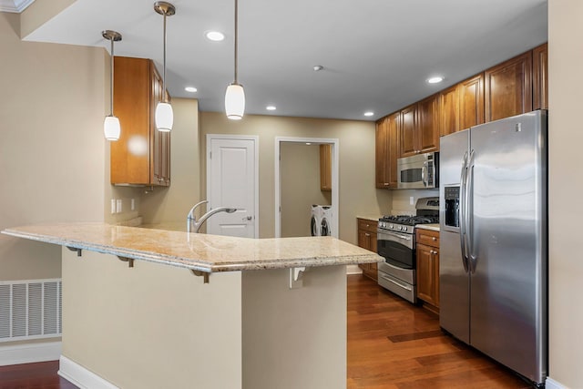 kitchen featuring visible vents, a breakfast bar area, decorative light fixtures, appliances with stainless steel finishes, and a peninsula