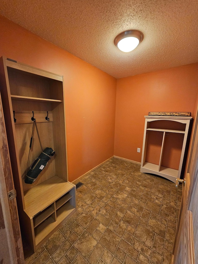 mudroom featuring a textured ceiling, stone finish flooring, visible vents, and baseboards