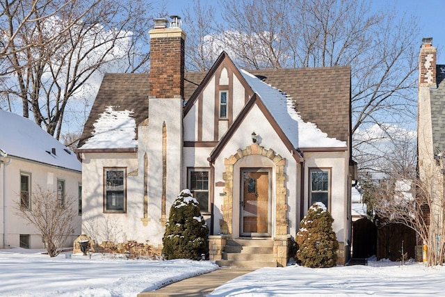 tudor house with roof with shingles, a chimney, and stucco siding