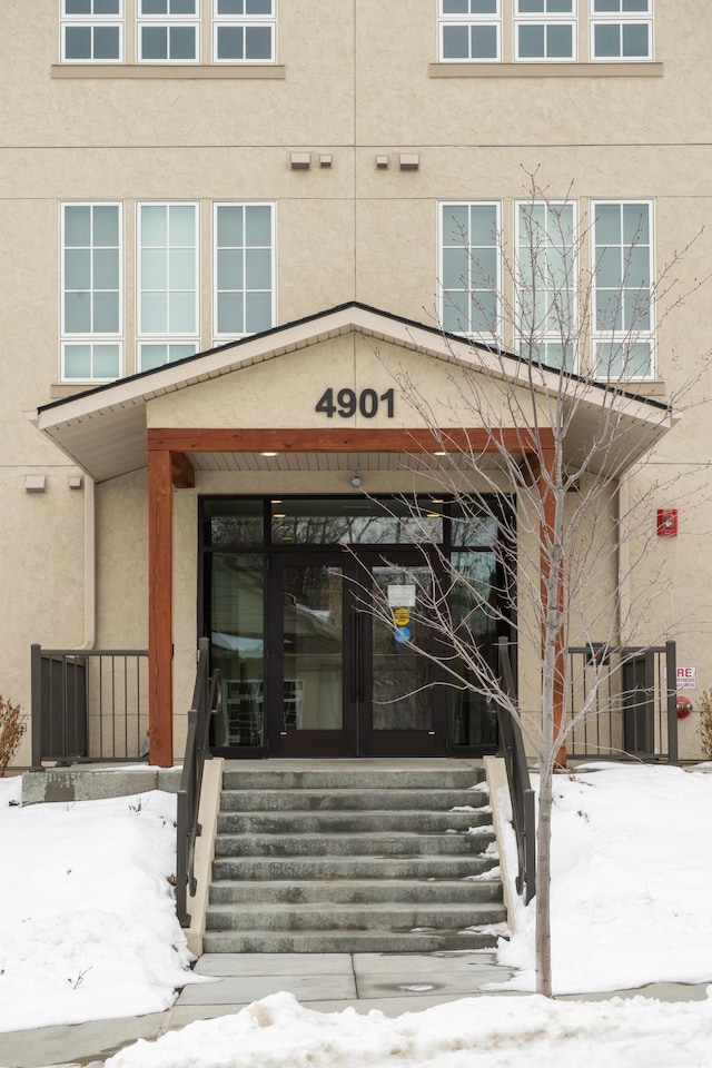 snow covered property entrance featuring stucco siding