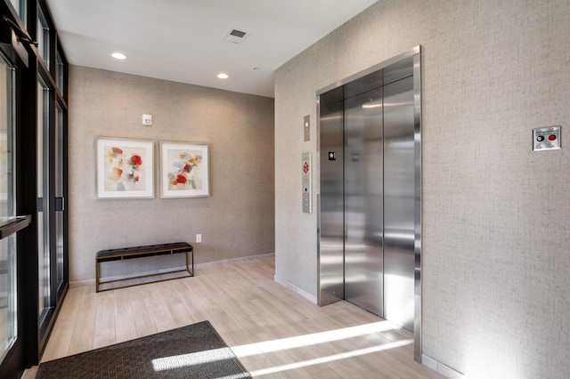 hall with light wood-type flooring, elevator, baseboards, and recessed lighting