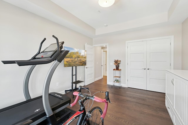 workout room featuring dark wood-style flooring, a raised ceiling, and baseboards