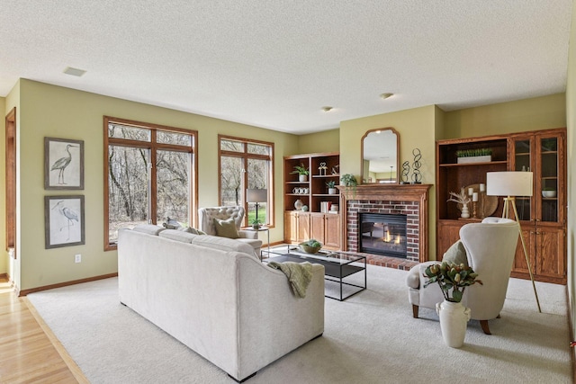 living area featuring a brick fireplace, a textured ceiling, baseboards, and wood finished floors