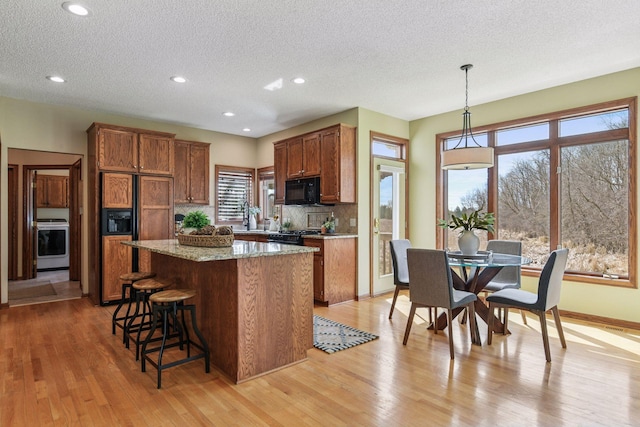 kitchen with a textured ceiling, brown cabinetry, tasteful backsplash, a kitchen island, and black appliances