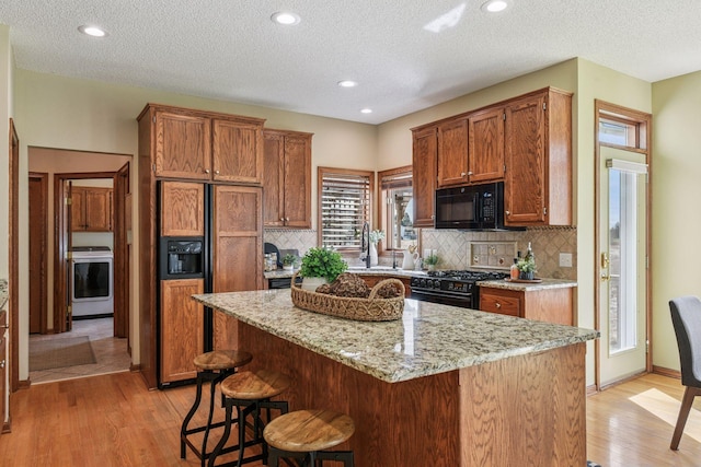 kitchen with washer / clothes dryer, a breakfast bar area, a center island, light wood-style flooring, and black appliances
