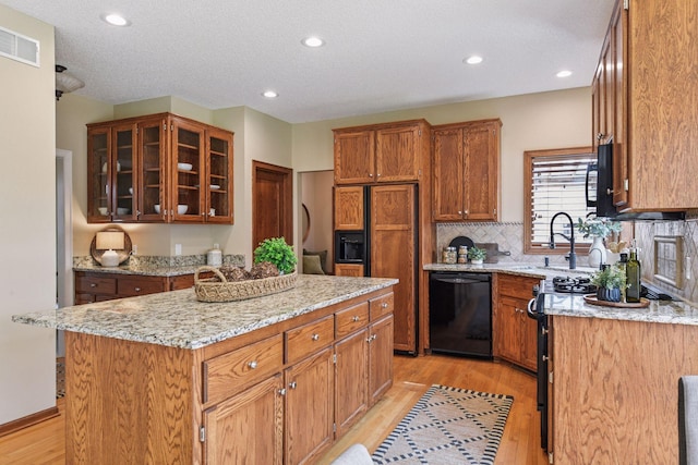 kitchen with visible vents, light wood-style floors, a kitchen island, and black appliances