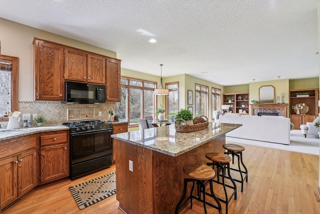 kitchen featuring light wood-style flooring, a textured ceiling, a breakfast bar area, and black appliances