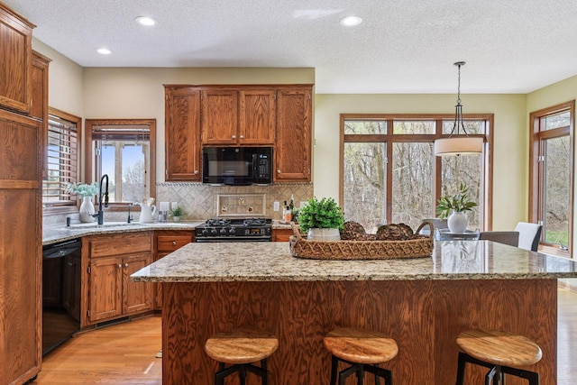 kitchen with a breakfast bar area, a textured ceiling, a sink, black appliances, and light wood-style flooring