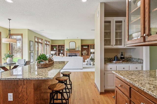 kitchen with light stone counters, a kitchen breakfast bar, a textured ceiling, light wood-style flooring, and decorative light fixtures
