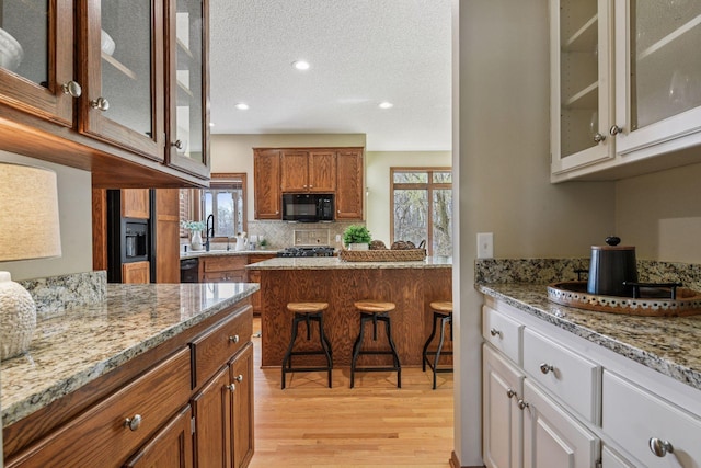 kitchen with brown cabinets, light stone counters, decorative backsplash, light wood-type flooring, and black appliances