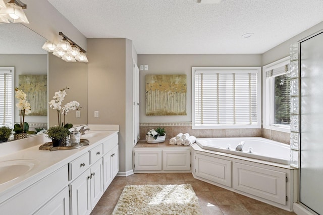 full bath featuring a textured ceiling, a sink, tile patterned flooring, and a garden tub