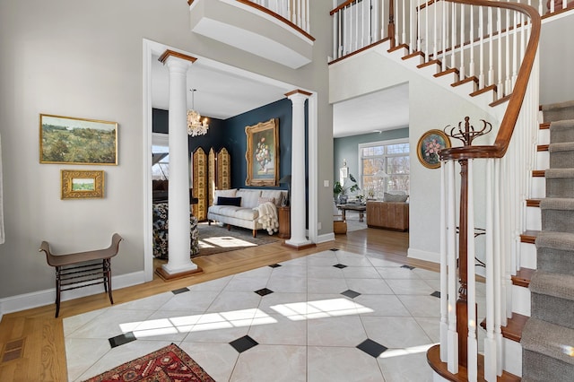 tiled entrance foyer with a notable chandelier, stairway, a high ceiling, baseboards, and ornate columns