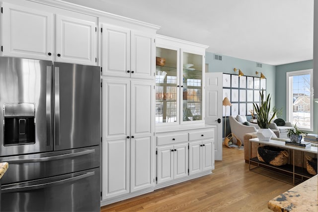 kitchen with light wood finished floors, visible vents, glass insert cabinets, stainless steel fridge with ice dispenser, and white cabinetry