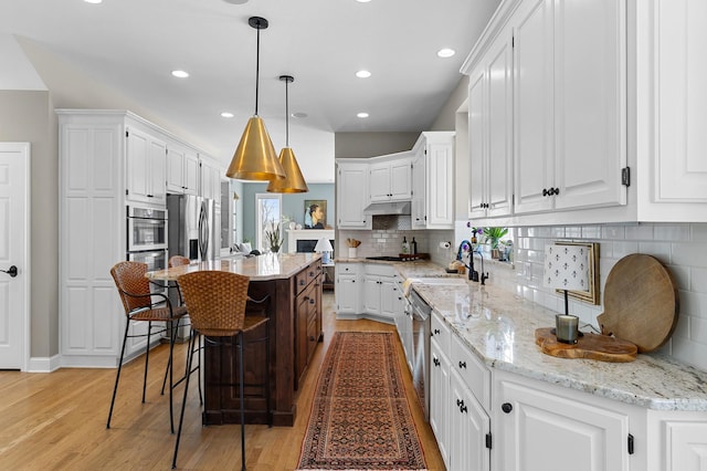 kitchen featuring light wood-style flooring, stainless steel appliances, white cabinets, under cabinet range hood, and a center island