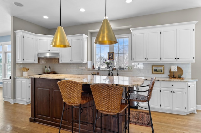 kitchen with a breakfast bar area, light wood-style flooring, white cabinets, pendant lighting, and a center island