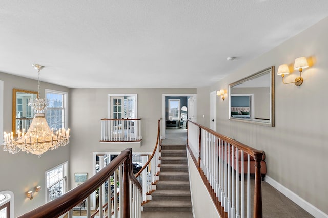 corridor with carpet flooring, a notable chandelier, an upstairs landing, and baseboards