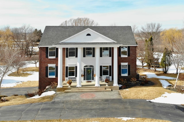 greek revival inspired property featuring brick siding, a porch, and a shingled roof