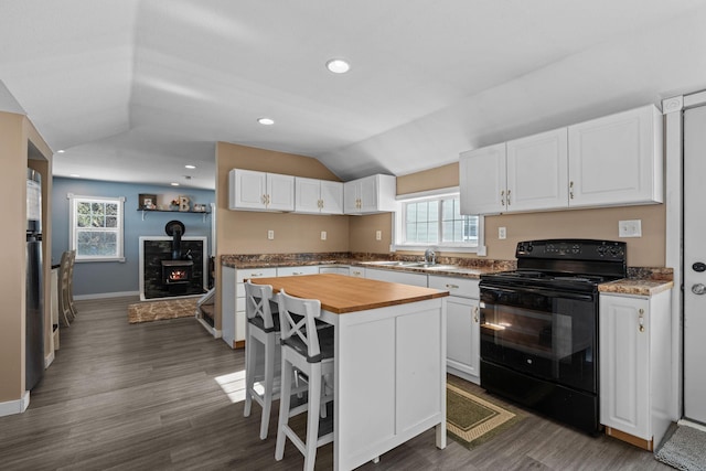 kitchen featuring electric range, white cabinets, a breakfast bar area, a center island, and vaulted ceiling