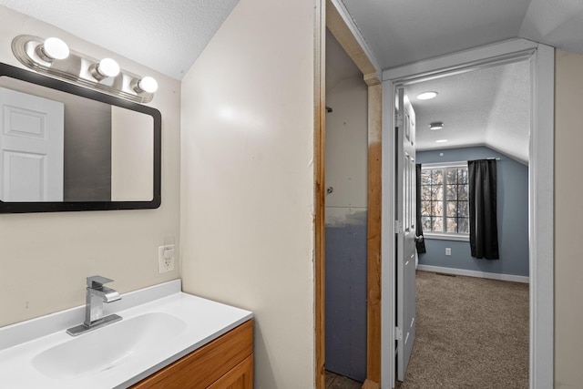 bathroom with baseboards, vaulted ceiling, a textured ceiling, and vanity