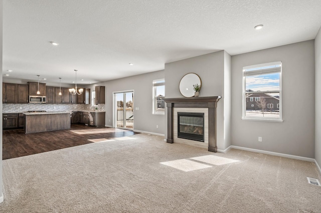 unfurnished living room featuring visible vents, a glass covered fireplace, dark colored carpet, baseboards, and a chandelier