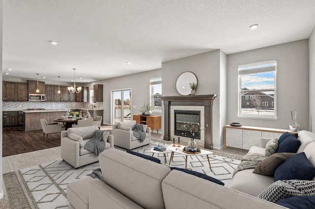 living area with recessed lighting, a chandelier, a healthy amount of sunlight, and a glass covered fireplace