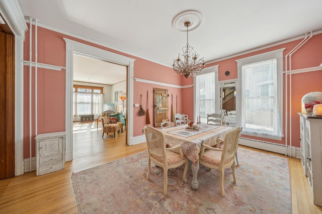 dining space featuring ornamental molding, light hardwood / wood-style floors, an inviting chandelier, and a baseboard radiator