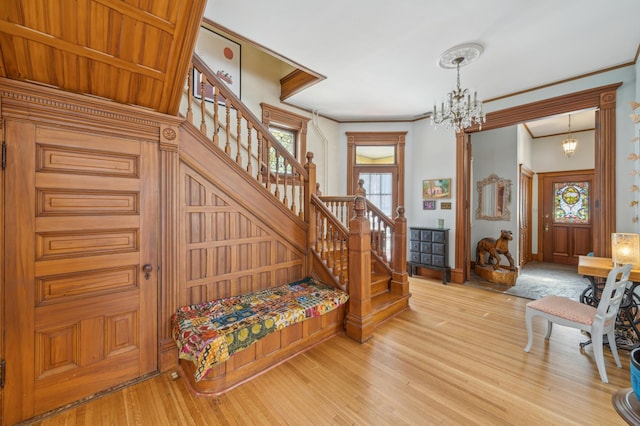 entrance foyer with an inviting chandelier, wood-type flooring, and ornamental molding