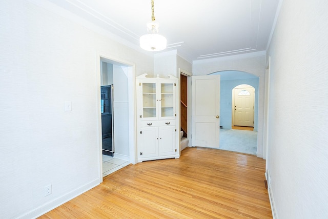 interior space featuring arched walkways, stairway, light wood-style flooring, ornamental molding, and baseboards