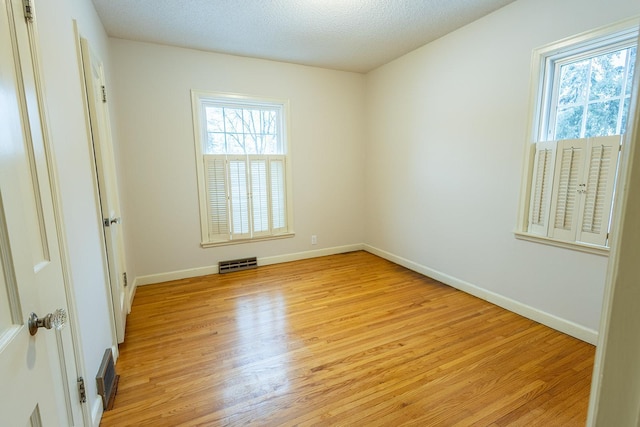 empty room with a textured ceiling, light wood-type flooring, visible vents, and baseboards