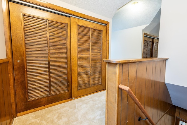 hallway with carpet floors, an upstairs landing, a textured ceiling, and lofted ceiling