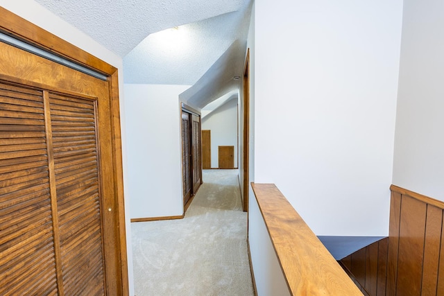 corridor featuring a wainscoted wall, carpet, vaulted ceiling, and a textured ceiling