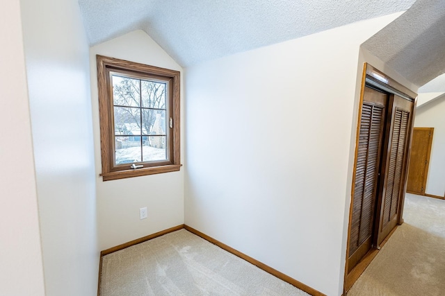 empty room featuring a textured ceiling, vaulted ceiling, baseboards, and light colored carpet